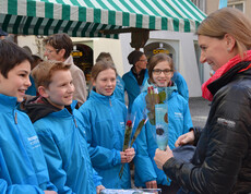 Eine junge Frau steht neben jungen Kindern und hält rote Rosen in der Hand. Die Kinder strahlen.