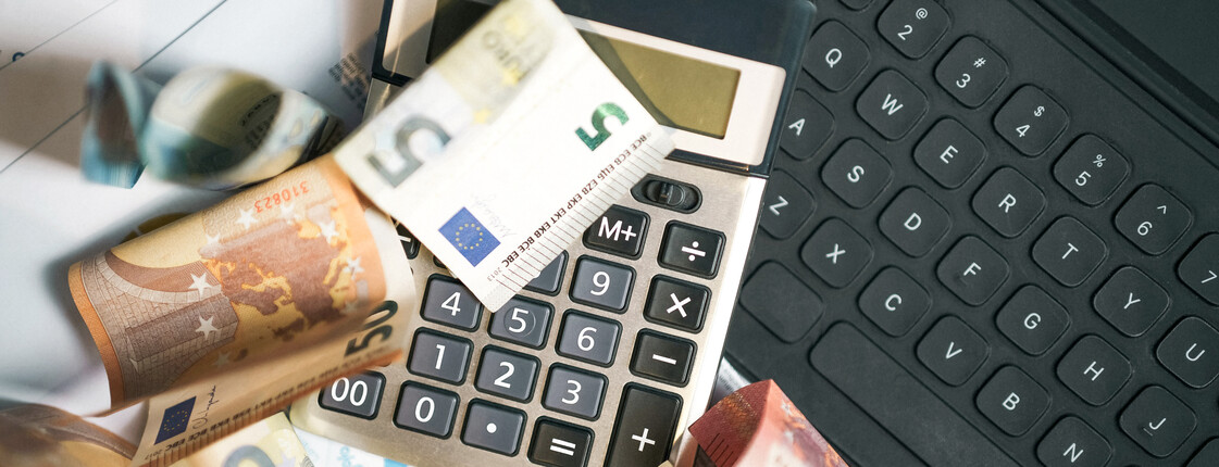Mehrere Euro-Banknoten liegen auf einem Taschenrechner neben einer Computertastatur.