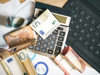 Mehrere Euro-Banknoten liegen auf einem Taschenrechner neben einer Computertastatur.