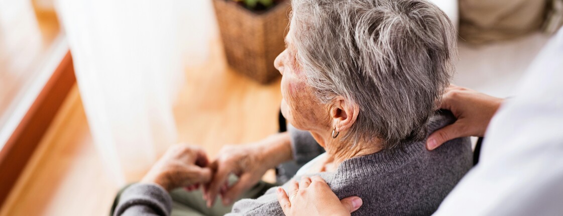 Pflegekraft begleitet eine ältere Person im Rollstuhl.