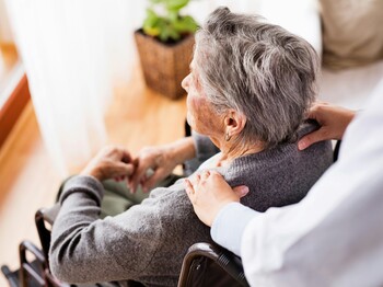 Pflegekraft begleitet eine ältere Person im Rollstuhl.