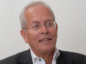 Ein älterer Herr trägt eine Brille und ein Sakko. 