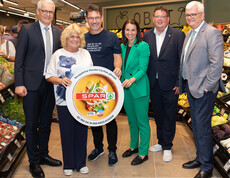 Große Gruppe in Supermarkt hält runde Tafeln mit SPAR-Logo und Caritas-Hinweis im Gang.