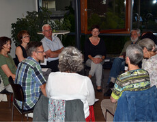 Eine Gruppe von etwa zehen Personen sind in einem Sitzkreis zusammengekommen. Dabei sind es überwiegend ältere Mitmenschen. 