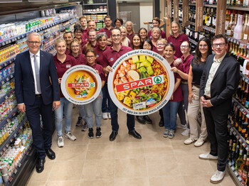 Große Gruppe in Supermarkt hält runde Tafeln mit SPAR-Logo und Karitas-Hinweis im Gang.
