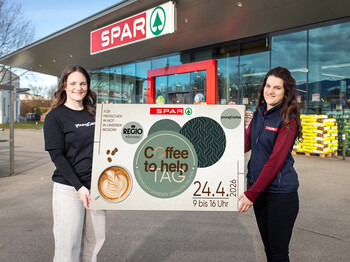 Zwei Frauen halten vor einem SPAR-Markt ein Plakat für den Coffee to help Tag am 24.4.2026 mit youngCaritas.