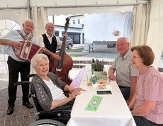 Zwei Musiker spielen für Gäste im Festzelt; Bewohner*innen und Angehörige sitzen gemeinsam am Tisch.
