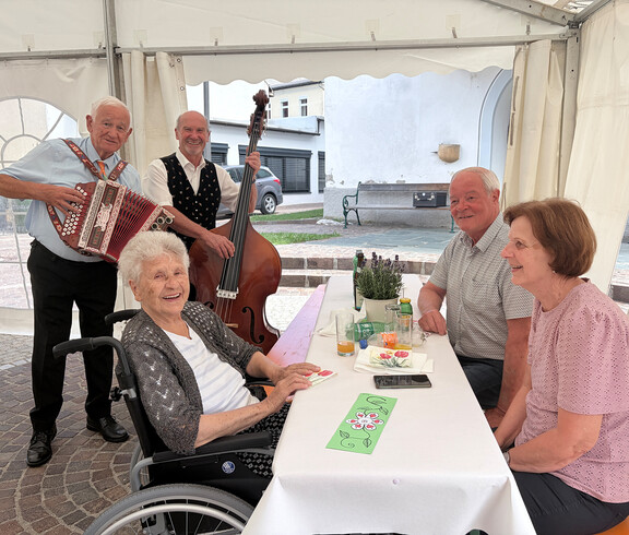 Zwei Musiker spielen für Gäste im Festzelt; Bewohner*innen und Angehörige sitzen gemeinsam am Tisch.