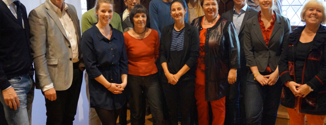 Einige Teilnehmer*innen der Integrationsgespräche der Caritas sind in einem Raum versammeln und posieren vor einem Banner der Caritas.