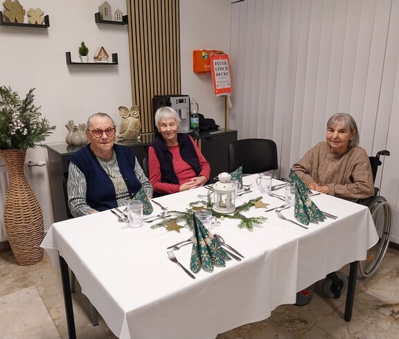 Bewohner*innen sitzen an festlich gedecktem Tisch mit Laterne und weihnachtlicher Deko