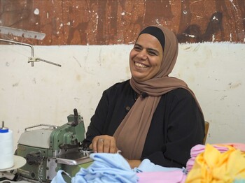 Eine ägyptische Frau mit einer Nähmaschine lacht herzlich.