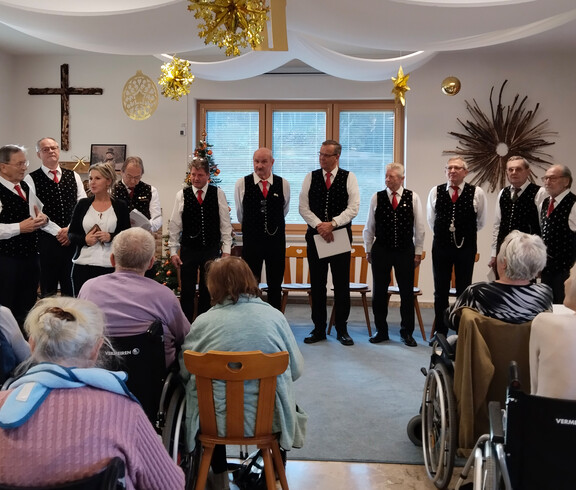 Gruppe von Sänger*innen vor Publikum, festlich gekleidete Gäste hören zu