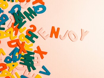 Bunte Holzbuchstaben liegen vertreut auf einem hellen Hintergrund und ein paar Buchstaben bilden das Wort 'enjoy'