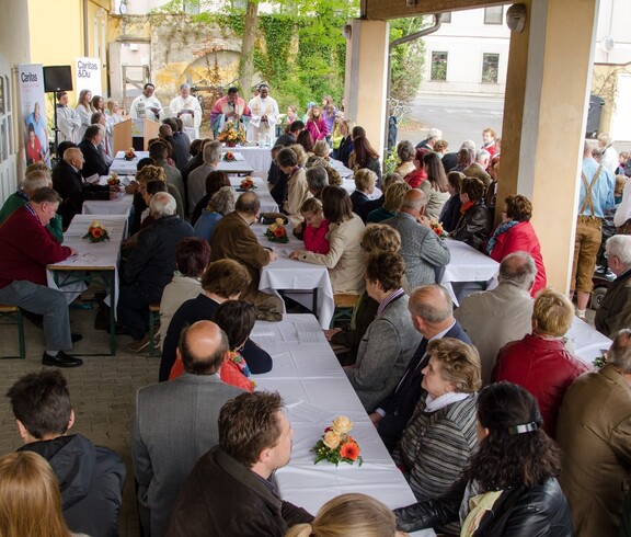 Viele Menschen sitzen bei Tischen und hören einem Gottesdienst zu.