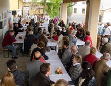 Viele Menschen sitzen bei Tischen und hören einem Gottesdienst zu.