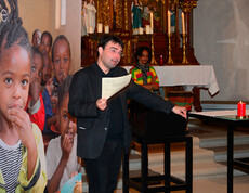 Ein Herr mittleren Alters mit gänzlich schwarzer Kleidung steht am Rednerpult der frastanzer Pfarrkirche. Der Hintergrund ziert eine großes Plakat von afrikanischen Kindern und einem afrikanischen Trommelspieler. 
