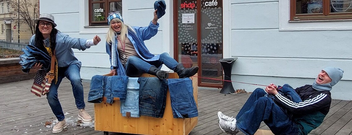 Drei Personen präsentieren vor einem Geschäft Jeans für eine Jeans-Aktion.