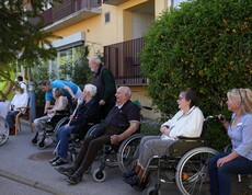 Mehrere Bewohnerinnen und Bewohner eines Pflegewohnhauses sitzen im Freien beisammen und verfolgen gemeinschaftlich das Geschehen rund um das festliche Maibaumaufstellen.