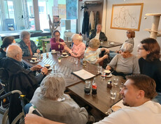 Gruppe von Bewohner*innen sitzt am Tisch im Katzencafé, trinkt Kaffee und tauscht sich während des Ausflugs aus