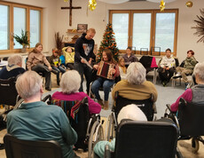 Gruppe von Senior*innen hört einem Kind mit Ziehharmonika zu