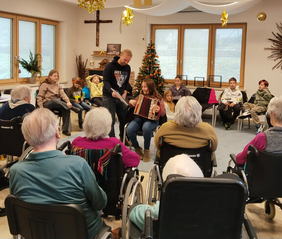Gruppe von Senior*innen hört einem Kind mit Ziehharmonika zu