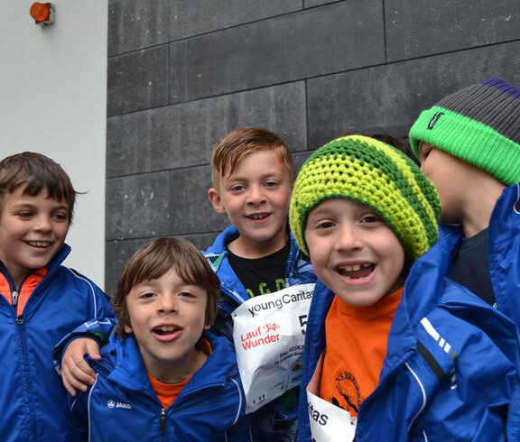 Etliche Kinder, die alle warm in blauen Winterjacken angezogen sind, manche tragen auch Mützen, stehen gemütlich zusammen zu einem Gruppenfoto. 