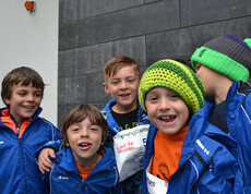 Etliche Kinder, die alle warm in blauen Winterjacken angezogen sind, manche tragen auch Mützen, stehen gemütlich zusammen zu einem Gruppenfoto. 