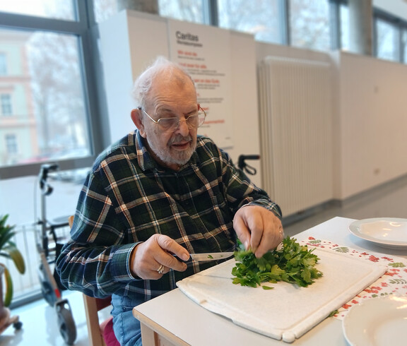 Ein Senior schneidet frische Kräuter an einem Tisch im Aufenthaltsraum.