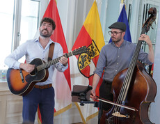 Zwei Musiker spielen Gitarre und Kontrabass vor Fahnen, im Raum eines Festakts