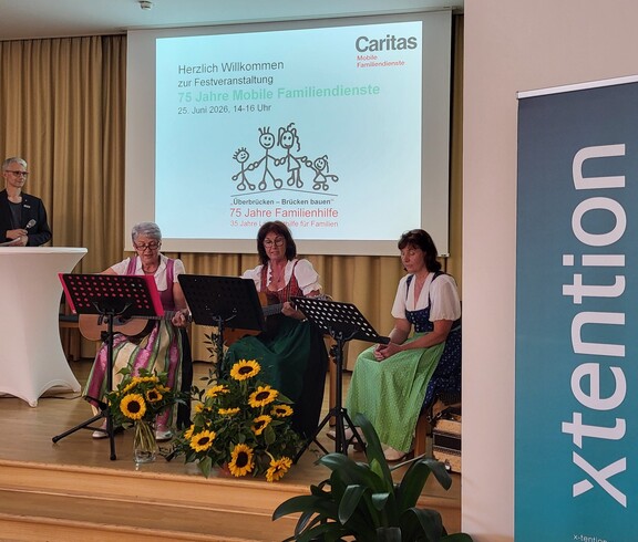 Drei Frauen sitzen mit Musikinstrumenten auf einer Bühne.
