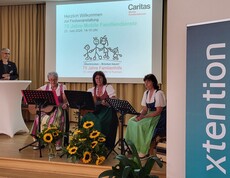 Drei Frauen sitzen mit Musikinstrumenten auf einer Bühne.