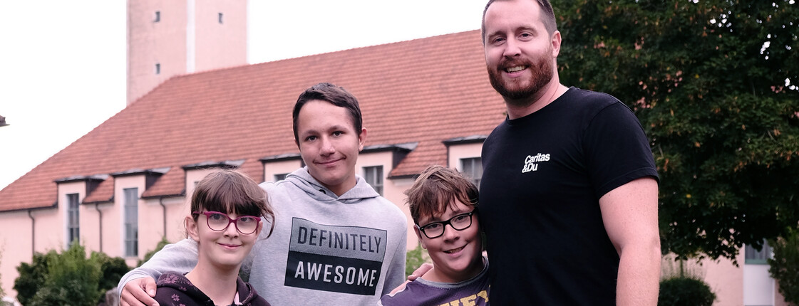 Ein Betreuer spielt Fußball mit drei Kindern vor der Kirche in St. Isidor.