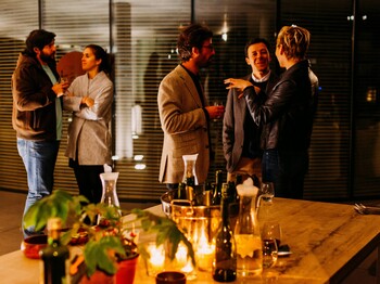 Fünf Personen stehen in gemütlicher Atmosphäre beisammen und unterhalten sich.