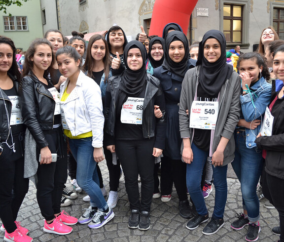 Ca. 15 Jugendliche und junge Erwachsene stehen in der feldkircher Innenstadt zu einem Gruppenfoto zusammen. Sie sind überwiegend dunkel gekleidet und manche junge Frauen tragen eine schwarze Kopfbedeckung. 