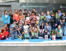 Kinder unterschiedlichen Alters stehen auf einer großen Landkarte, die den ganzen Globus repräsentiert. In der Mitte steht ein Bub, der ein ORF Mikrofon in der Hand hält. 