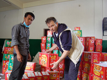Zwei Männer unterschliedlicher Nationalitäten tragen Lebensmittelpakete ins Lager. Ein Mann hält gerade ein solches in der Hand. 