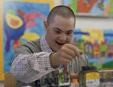 Mensch mit Behinderung widmet sich völlig dem Malen mit Aquarellfarben. Freude steht ihm im Gesicht. 