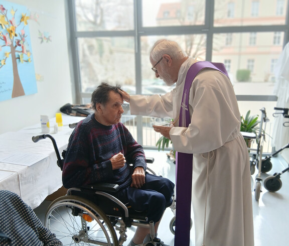 Priester gibt einer Person im Rollstuhl das Aschenkreuz während der Messe im Haus Martha.