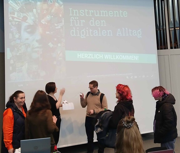 Sechs Menschen diskutieren vor einer Videowand.